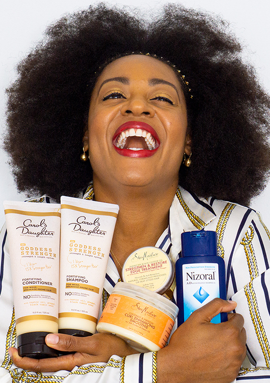 woman with afro hold hair products laughing.