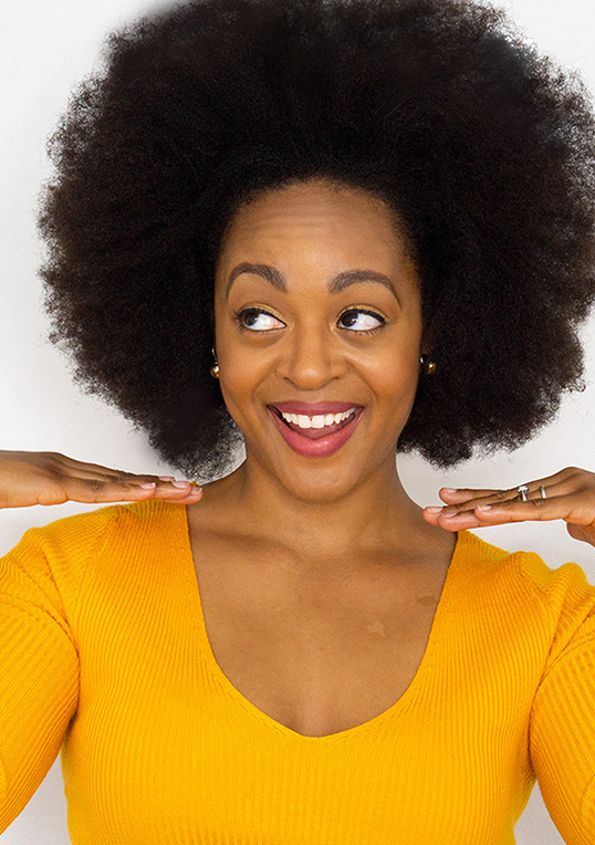 woman with big afro wearing yellow v neck smiling
